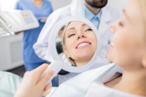 Imagen mujer joven sonriendo delante de un espejo después de un tratamiento dental.